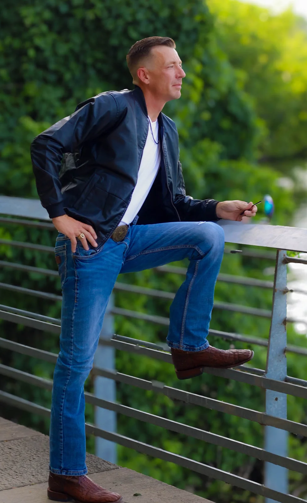 Man in the black Summit Classic Bomber leaning on a riverside bridge rail